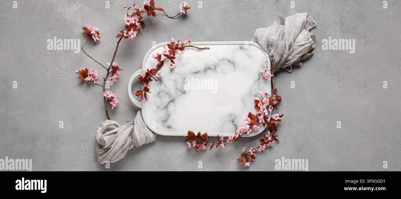Weißes Marmor-Serviertablett mit rosa Kirschblütenzweigen und grauem Stoff auf einem Betonhintergrund, diese elegante Flat-Lay-Komposition bietet reichlich Stockfoto