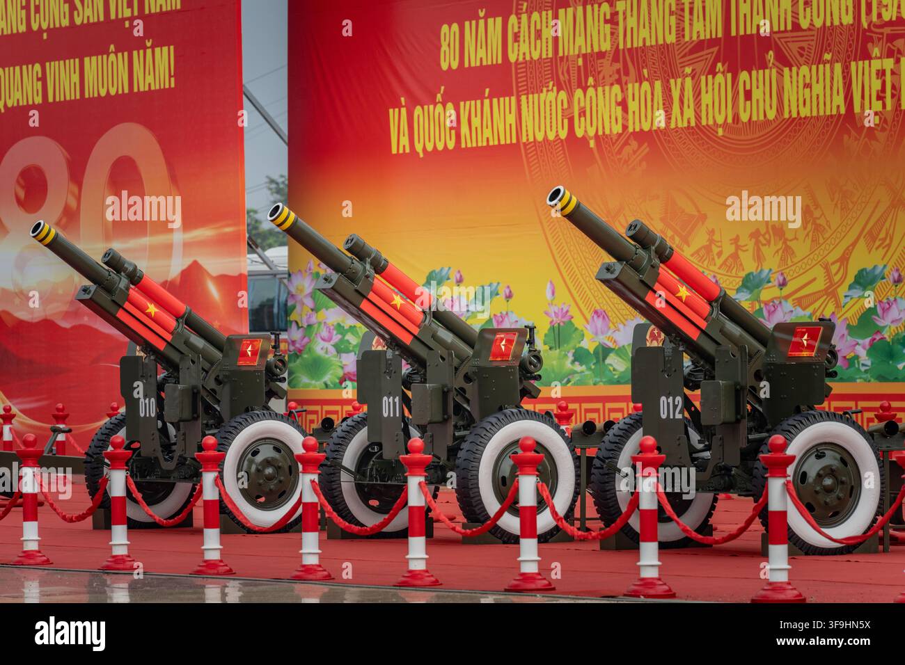 Zeremonielle Artilleriegewehre aufgereiht vor rotem Jubiläums-Hintergrund, My Dinh Stadium, Hanoi Stockfoto