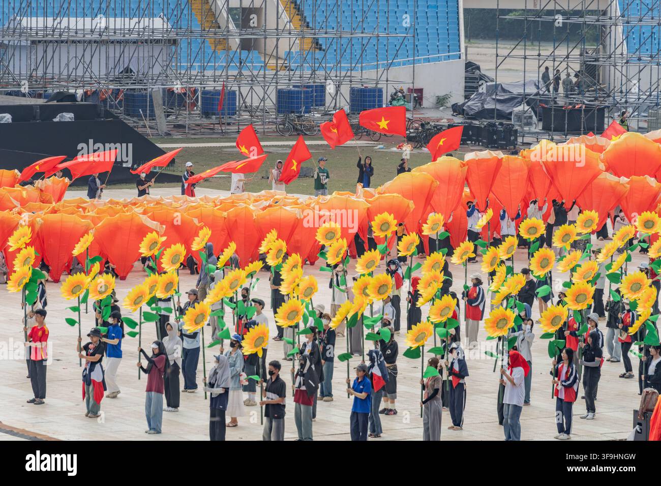 Erhöhte Ansicht einer Massenprobe mit Sonnenblumen-Requisiten und orangefarbenen Fächern auf dem Stadionfeld, My Dinh Stadium, Hanoi Stockfoto