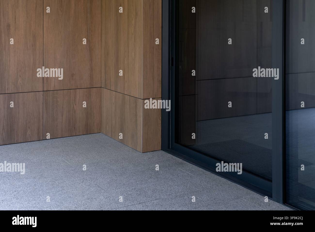 Moderne Eingangsecke mit Holzverkleidung und dunkler Glasschiebetür, Nahaufnahme des zeitgenössischen Gebäudeexterieurs Stockfoto
