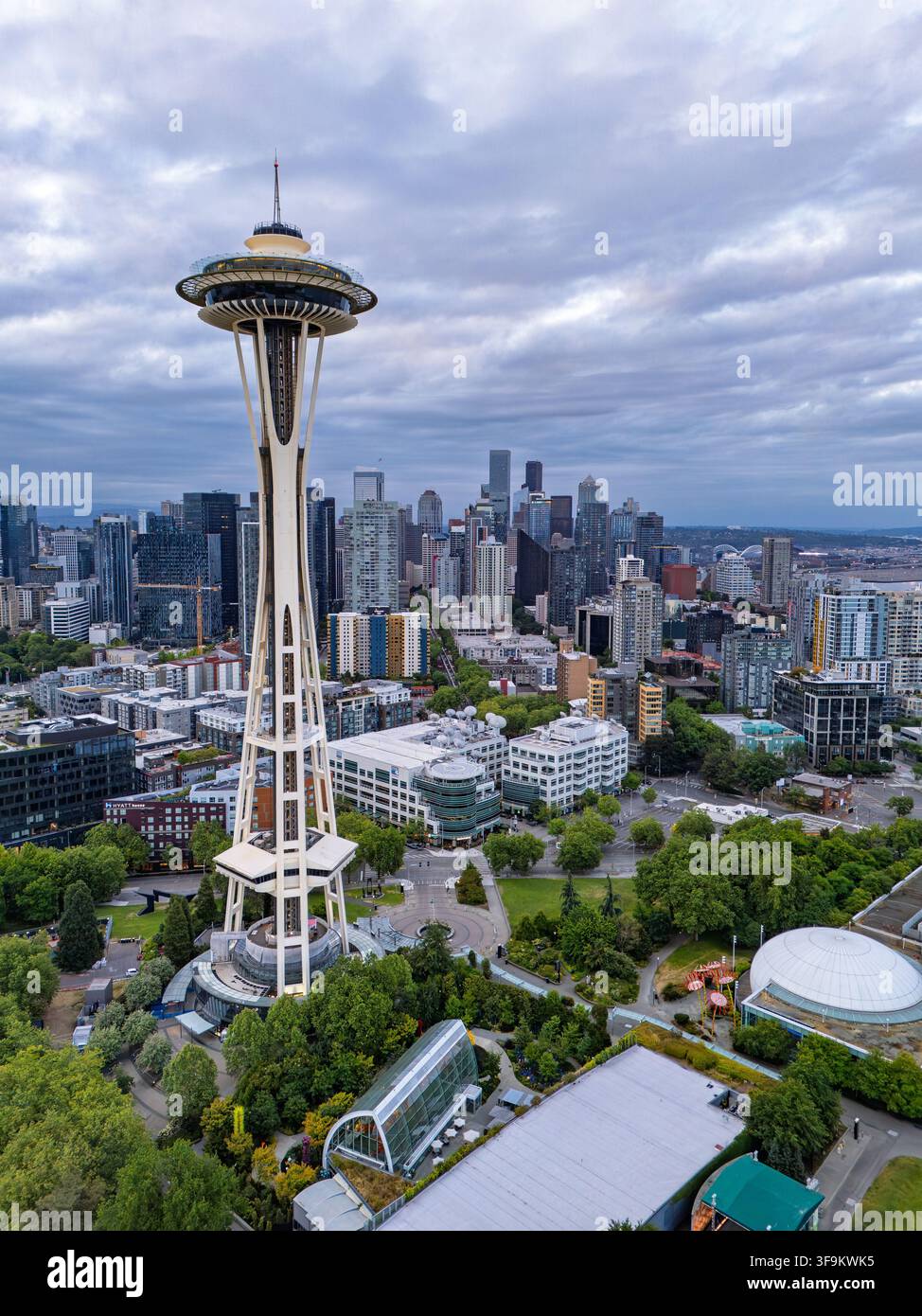 Blick auf die Space Needle, die über der Skyline von Seattle aufragt, mit umliegenden städtischen Gebäuden, üppigen grünen Bäumen und einem bewölkten Himmel in Seattle, Washington Stockfoto
