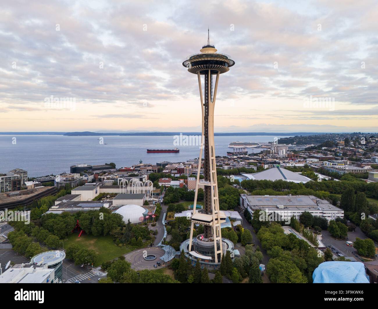 Blick auf die Space Needle, die über dem Seattle Center Park aufragt, mit dem Puget Sound und einem Frachtschiff im Hintergrund in Seattle, Washington, Vereinigte Staaten Stockfoto