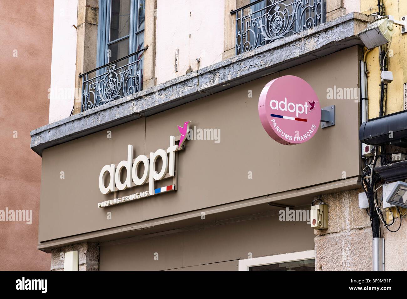 Macon, Frankreich - 01. August 2026: Schaufensterzeichen und rundes Logo des Parfümladens Adopt Parfums Francais an der Wand eines historischen Gebäudes. Stockfoto