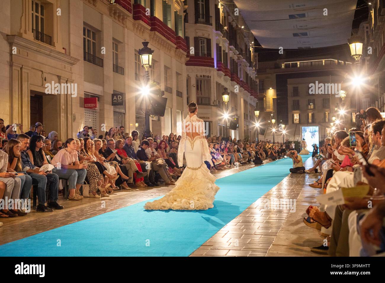 Málaga, Spanien, 13. September 2024. Model in einem eleganten weißen Kleid geht über den beleuchteten Laufsteg während der Pasarela Larios Málaga Fashion Week auf der Calle Lari Stockfoto