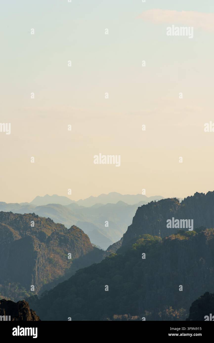 Bewaldete Karstkämme ziehen sich durch atmosphärischen Dunst unter einem weiten blassen Himmel zurück und schaffen eine starke natürliche Tiefenwirkung und großzügigen Kopierraum. Stockfoto