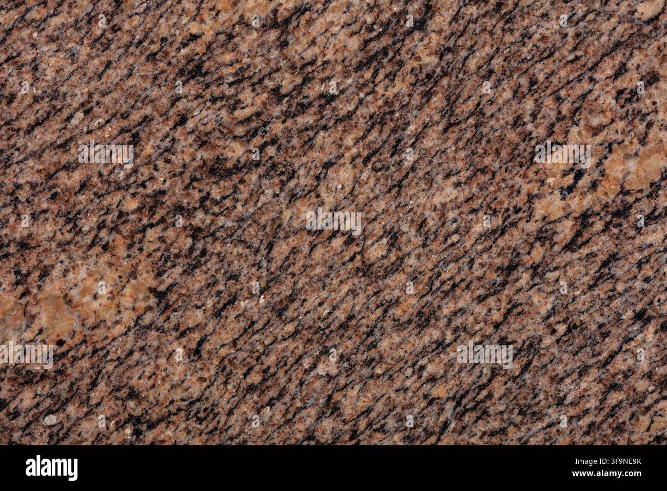 Vollformat-Nahaufnahme einer polierten Granitplatte in warmen Brauntönen, die diagonale dunkle Adern und kristalline Sprenkel über den Naturstein zeigt Stockfoto