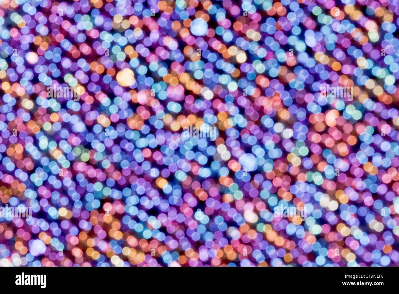Unscharfe Lichter bilden sich überlappende runde Bokeh-Punkte in violetten, blauen und warmen Orangetönen und erzeugen eine vollflächige abstrakte Textur mit einem festlichen Schimmer Stockfoto