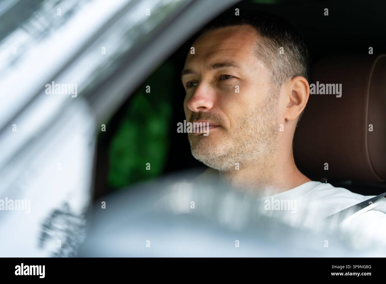 Mittelalter Mann fährt ein Auto und schaut durch die Windschutzscheibe nach vorne, Nahaufnahme-Porträt eines konzentrierten Fahrers in einem modernen Fahrzeug. Stockfoto