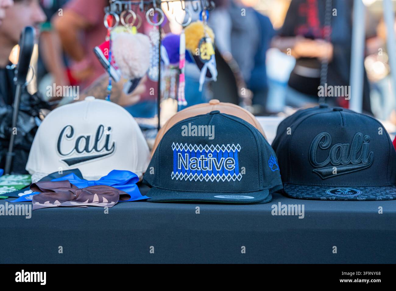 Baseballmützen mit der Aufschrift „Cali“ und „Native“, die zum Verkauf auf einem Verkaufstisch im Heart Health Park während der Native American Heritage Night ausgestellt sind. Stockfoto
