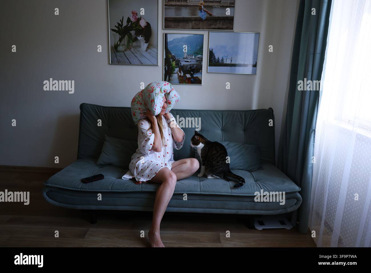 Müde Frau ruht sich auf der Couch aus mit Kissen über dem Kopf und einer Hauskatze neben ihr, überfordert und erschöpft zu Hause Stockfoto