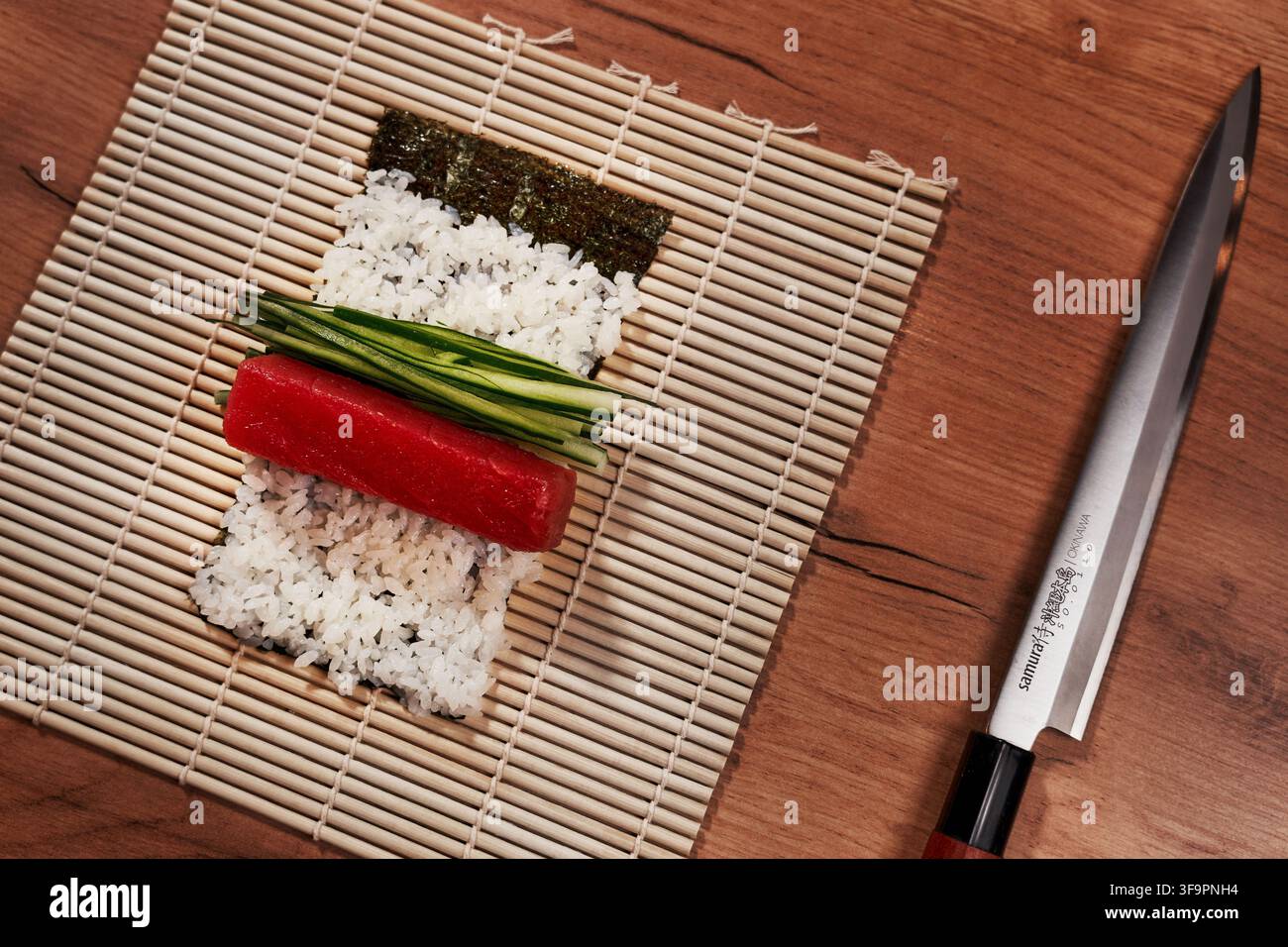 Sushi-Zubereitung mit frischem Thunfisch, Gurke und Reis auf Bambusmatte mit japanischem Kochmesser Stockfoto