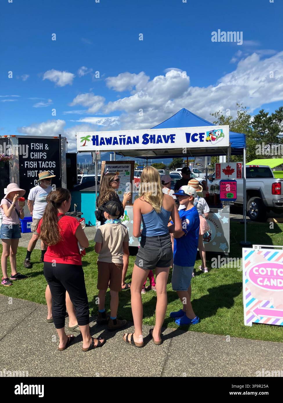 Menschen stehen an einem Hawaiian Shave Ice Essensstand an einem sonnigen Sommertag während der Nautical Days in Comox, British Columbia, Kanada. - Smartphone-aufgenommenes Stockfoto