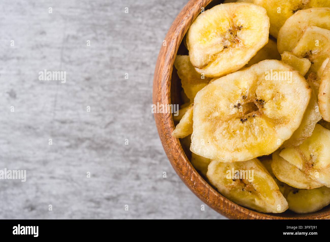 Knusprige Bananenchips in einer Holzschale auf grauem Hintergrund Stockfoto