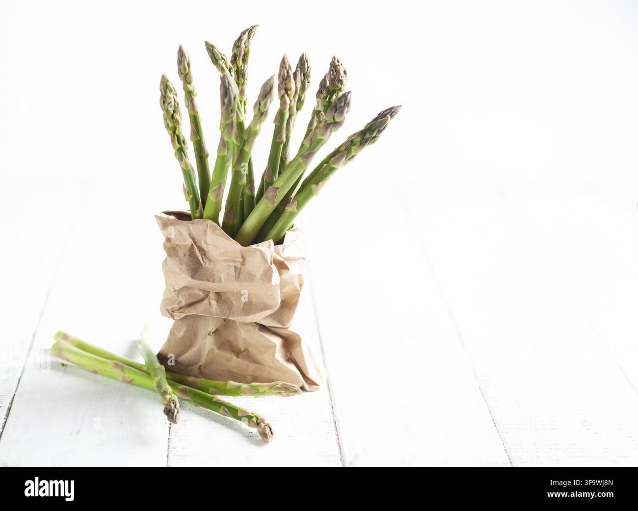 Ein Bündel grüner Spargel in einer Papiertüte auf einem weißen Holztisch. Konzept für gesundes Essen, frisches Gemüse Stockfoto