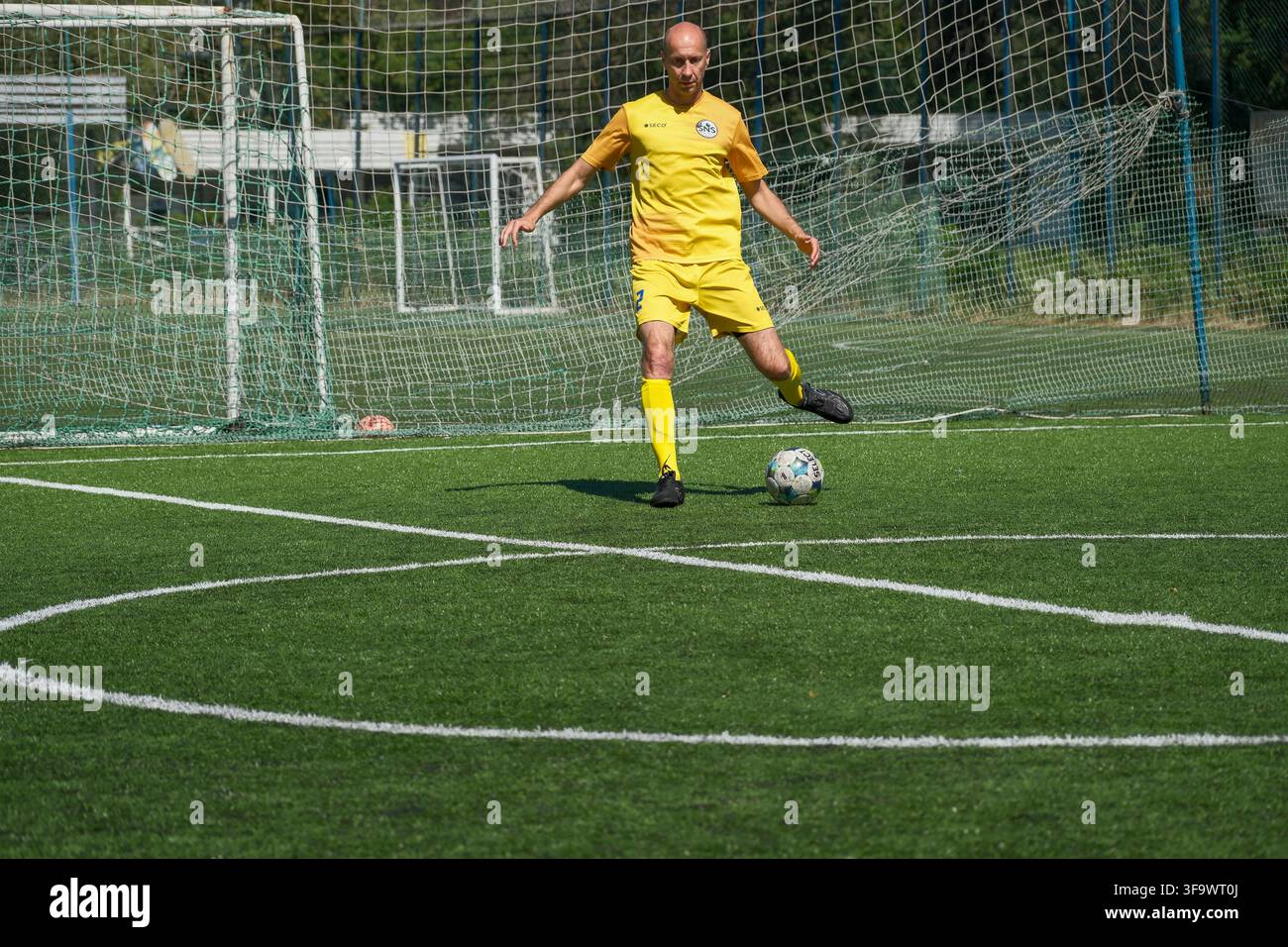 KIEW, UKRAINE - 17. AUGUST 2026: Ein Amateur-Mini-Fußballspieler in einem gelben Trikot schießt einen Select-Fußball von der weißen Linie des Mittelkreises Stockfoto
