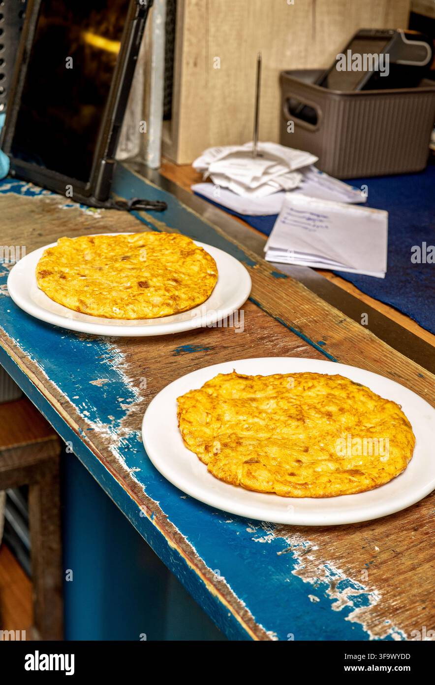 Individuelle spanische Omeletts auf weißen Tellern, die auf einer rustikalen Holztheke in einem lokalen Restaurantkontext ruhen. Stockfoto