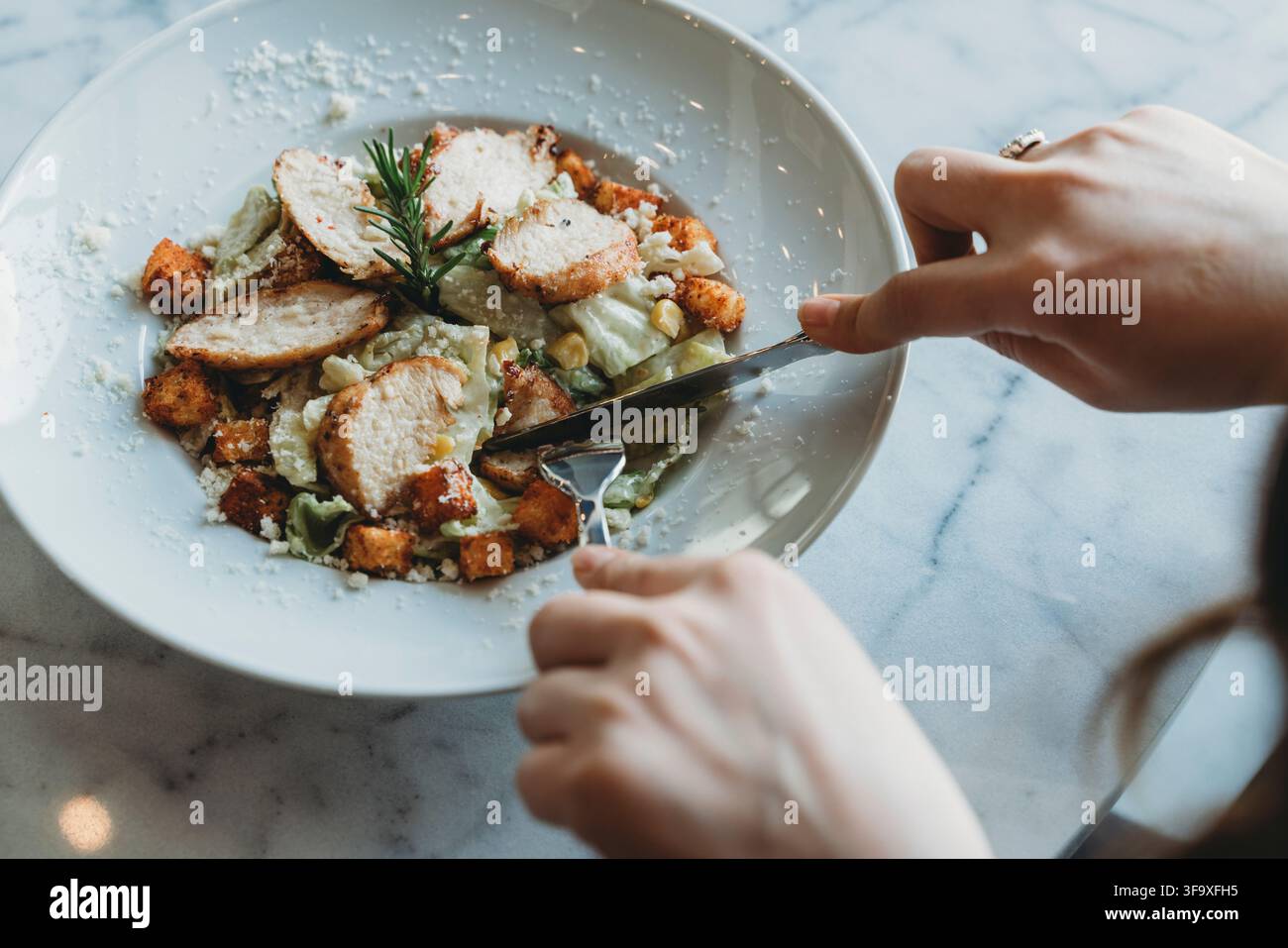 Frau schneidet gegrilltes Hühnchen auf einem Caesar-Salat Stockfoto
