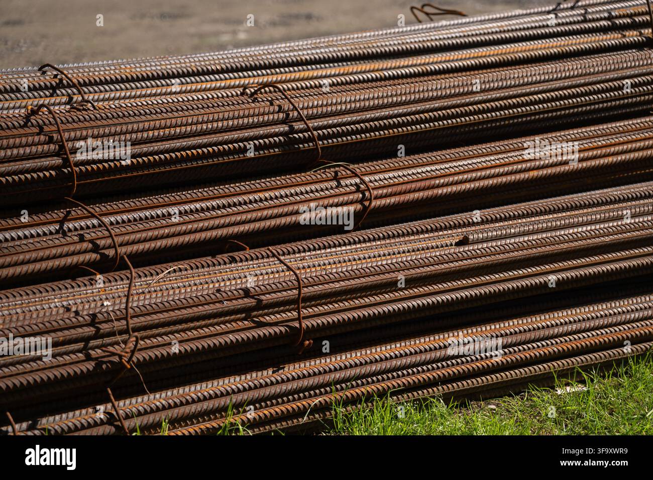 Gestapelte Bündel rostiger Stahlbügel, die auf dem grünen Gras liegen, repräsentieren Materialien für Baustellen und Industrie-Infrastrukturprojekte Stockfoto