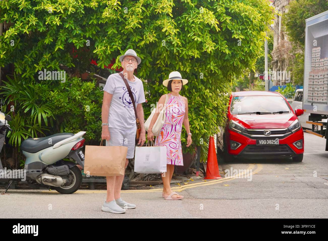 Seniorenpaar mit Hüten und Einkaufstüten, das auf einer städtischen Straße in George Town Penang, Malaysia, steht Stockfoto