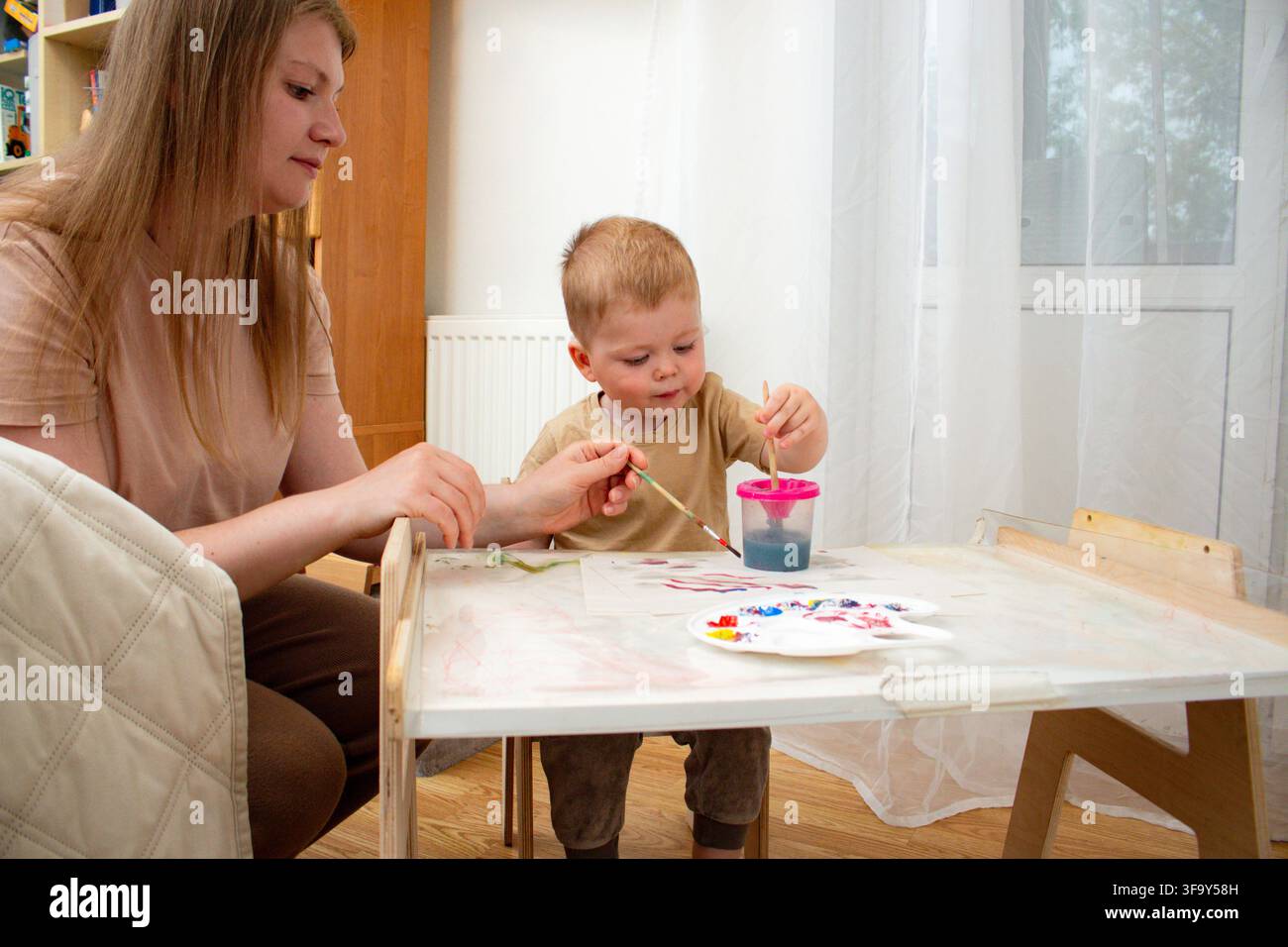 Kleinkind malt mit Pinsel und Händen. Sensorische Stimulation durch nasse Farbe. Unabhängiges kreatives Spielen. Taktiles Wissen durch Berührung Stockfoto