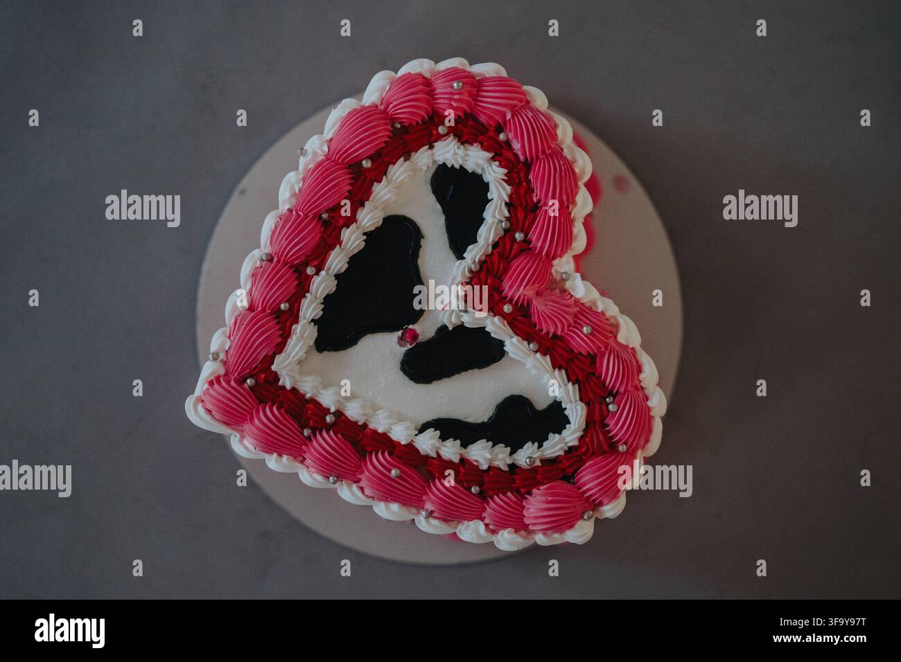 Herzförmiger Geburtstagskuchen mit rosa Zuckerguss und weißer Glasurdekoration auf dem Teller Stockfoto