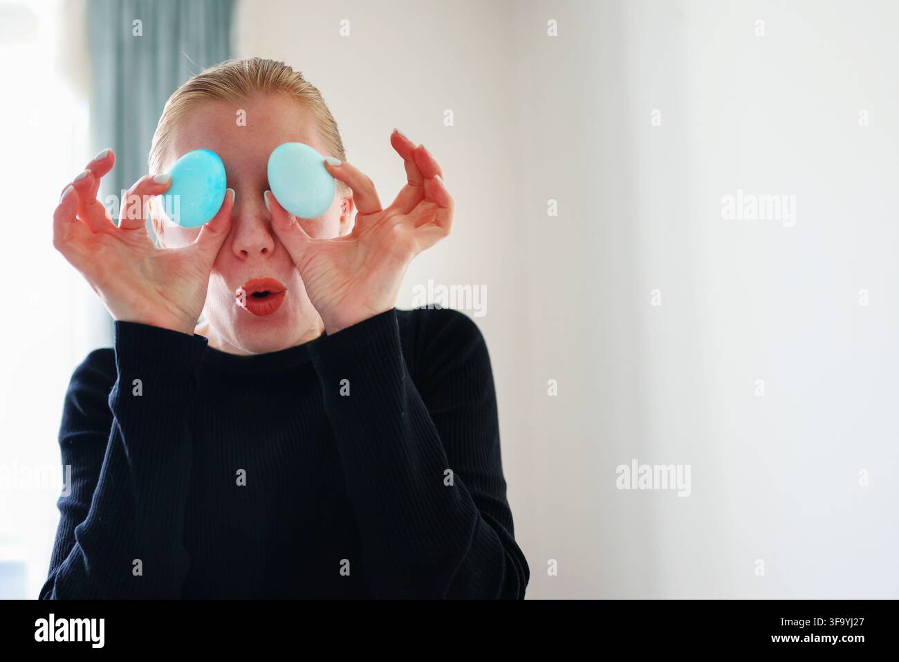 Verspielter Ostermoment, Frau verwendet Eier als Brille, helle Lebensstil-Szene. Stockfoto