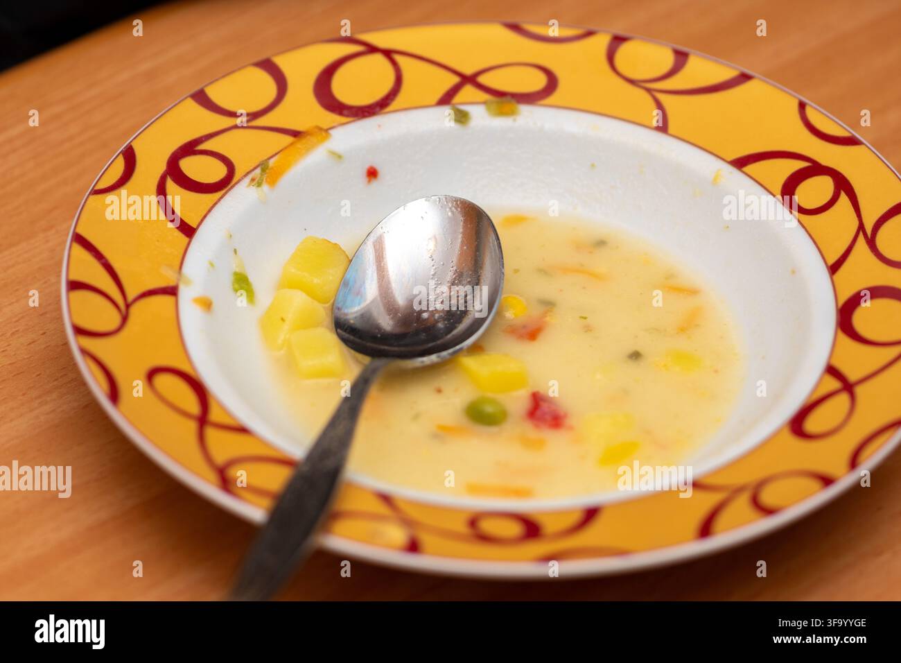 Ein Löffel ruht in einer Schüssel mit teilweise aufgegessener cremiger Gemüsesuppe auf einem Holztisch. Stockfoto