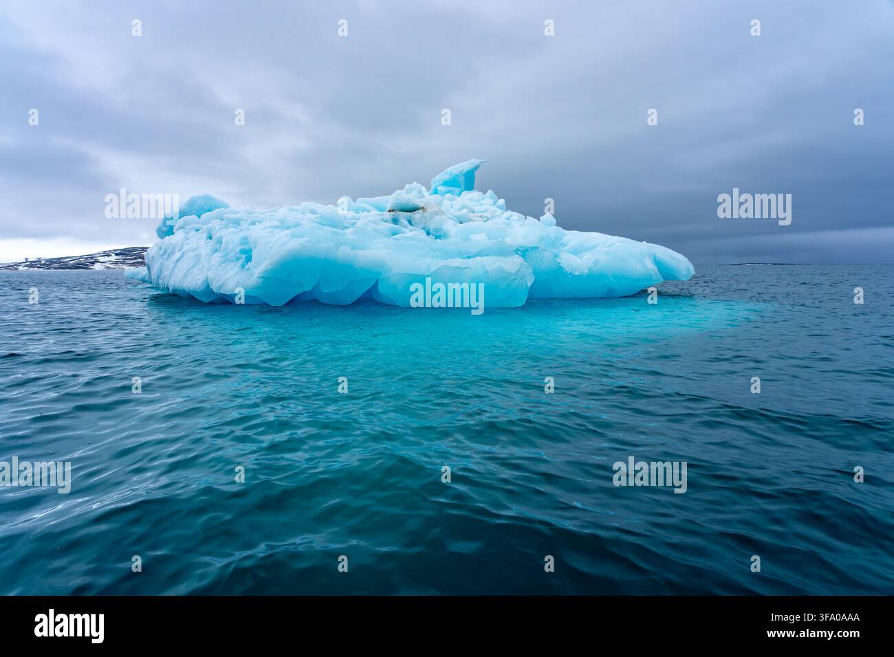 Blauer Eisberg schwimmt in tiefblauem Ozeanwasser unter einem dramatischen grauen Himmel und zeigt die fragile Schönheit der polaren Umgebungen und repräsentiert das On-Going Stockfoto