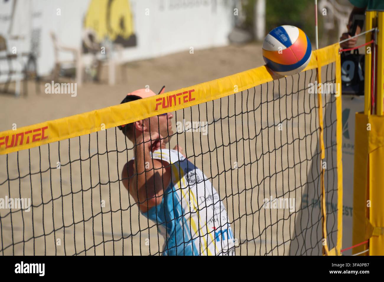 KIEW, UKRAINE – 16. AUGUST 2026: Ein Amateur-Strandvolleyballspieler beobachtet aufmerksam den Ball, der auf dem Rand des gelben Funtec-Netzes balanciert. Thi Stockfoto