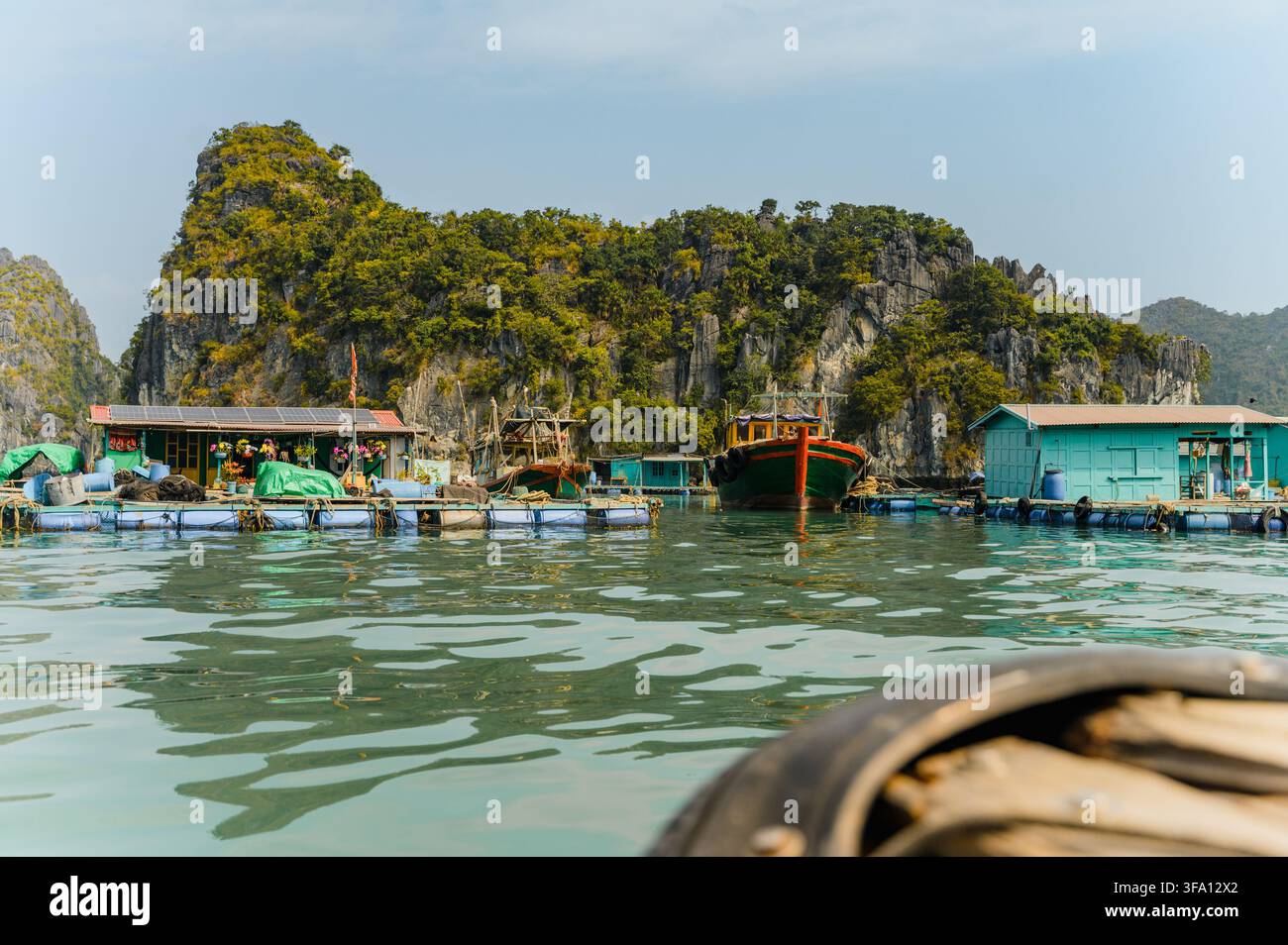 Traditionelle schwimmende Dorfhäuser und Fischerboote ruhen neben einer üppigen Kalksteininsel in der Lan-Ha-Bucht, Cat-Ba-Archipel, Hai Phong, Vietnam. Stockfoto