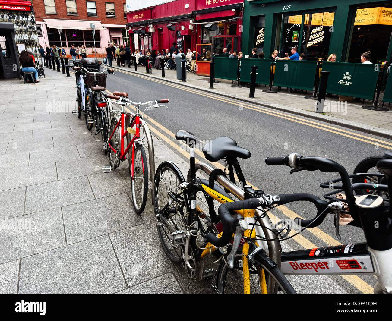 Dublin, Irland – 22. Mai 2026: Geparkte Fahrräder säumen eine belebte Straße in Dublin mit Straßencafés, Restaurants und einer urbanen Atmosphäre. Stockfoto