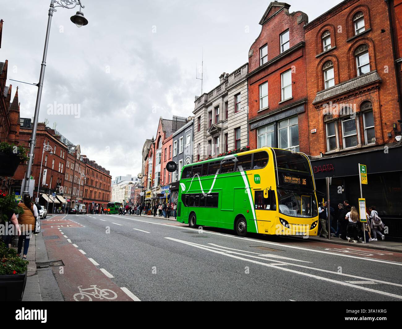Dublin, Irland – 22. Mai 2026: Grüner Doppeldeckerbus an einer überfüllten Stadtbushaltestelle vor historischen roten Backsteinläden in Dublin, Irland. Stockfoto