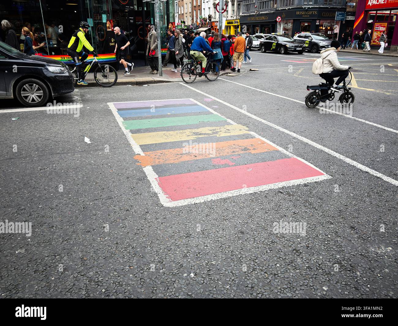 Dublin, Irland – 22. Mai 2026: Regenbogen-LGBT-Fußgängerüberweg auf einer belebten Straße in Dublin mit Radfahrern, Fußgängern, Verkehr und farbenfrohen urbanen Ladenfronten. Stockfoto