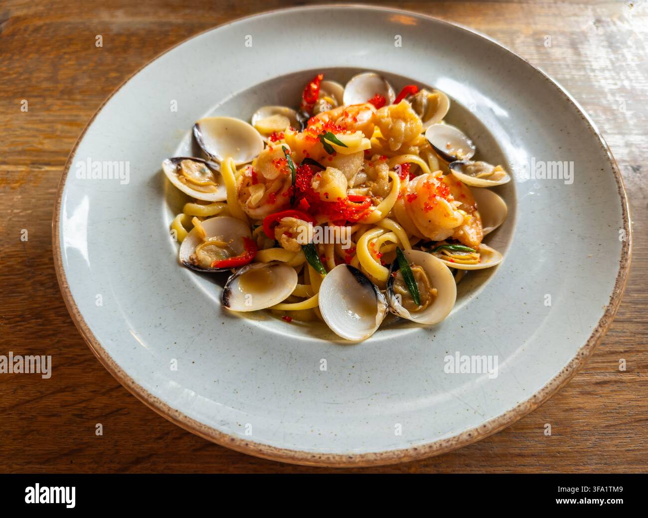 Meeresfrüchte-Linguine-Pasta-Gericht mit frischen Muscheln, Garnelen, Tintenfisch, rotem Rogen und Chili, serviert auf einem hellen Teller Stockfoto