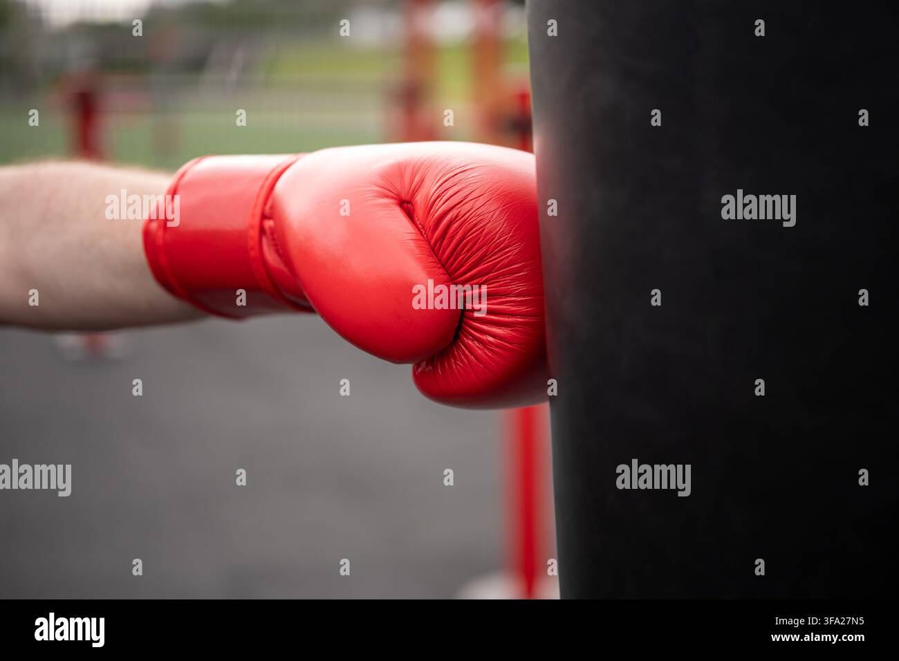 Roter Boxhandschuh schlägt einen schweren Sack während eines Outdoor-Workouts Stockfoto