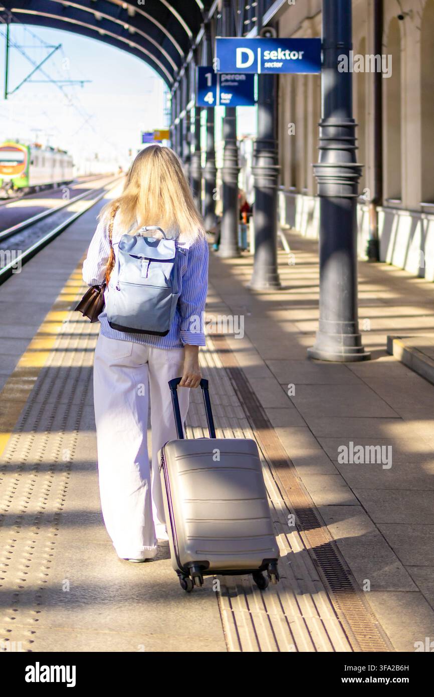 Reife Frau geht von der Kamera weg in Richtung Bahnsteig und zieht einen Rollkoffer hinter sich her. Konzept von Solo-Geschäftsreisen und unabhängiger Reise Stockfoto