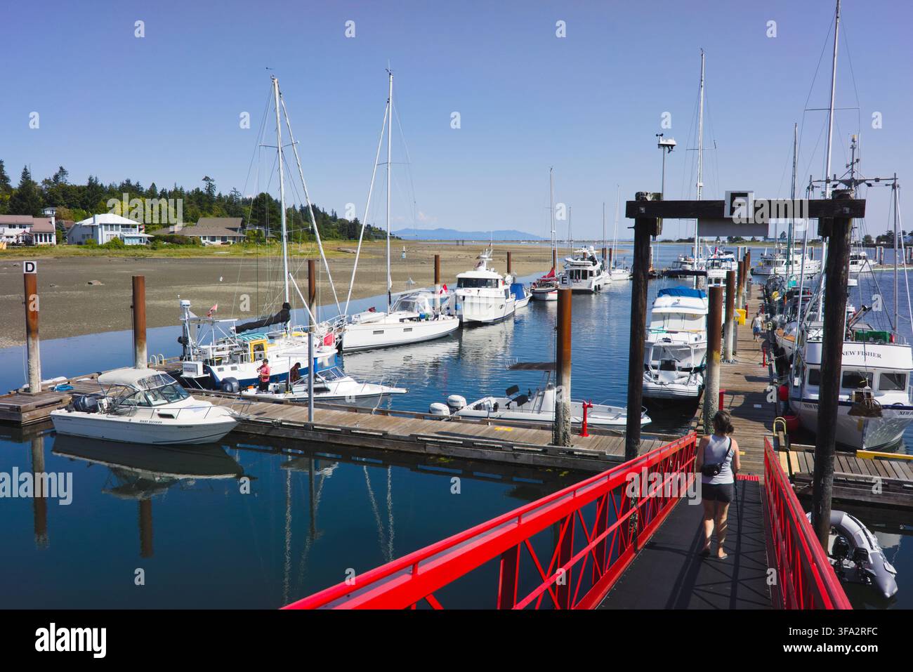 Roter Steg, der zu den Docks hinunterführt, mit festgemachten Yachten und Segelbooten im Comox Marina in Comox, Vancouver Island, British Columbia. Stockfoto