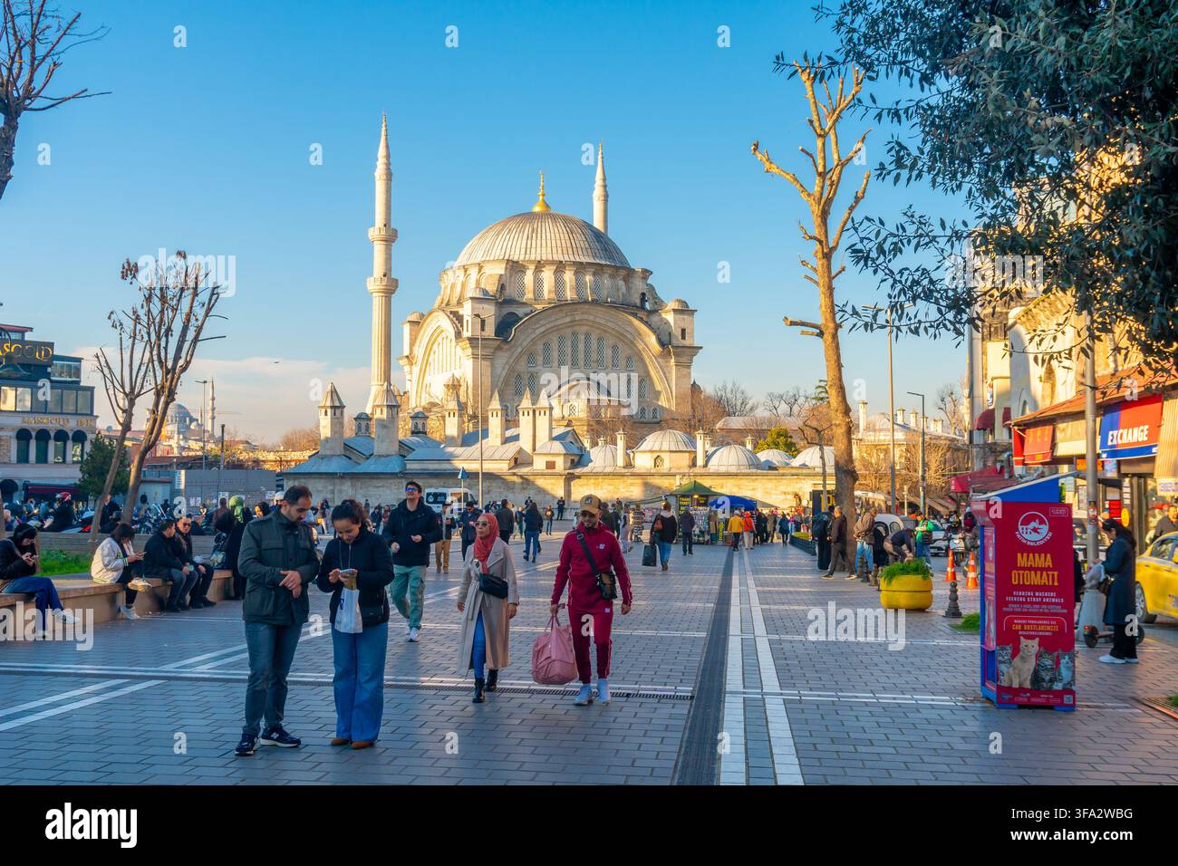 Istanbul, Türkei – 10. Januar 2025: Eine geschäftige Straßenszene entfaltet sich unter einem klaren blauen Himmel und zeigt die architektonische Pracht einer großen Moschee a Stockfoto