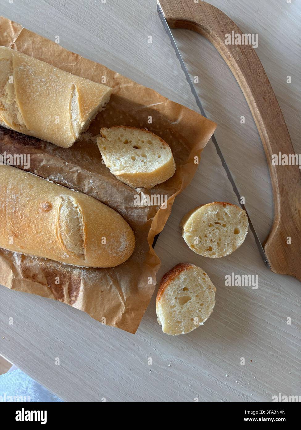 Geschnittenes frisches Baguette und Küchenmesser auf Holzschneidebrett, rustikales Frühstücks- oder Bäckereikonzept. Hochwertiges Foto Stockfoto