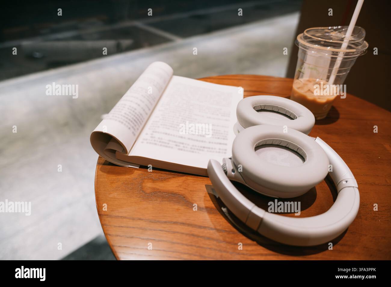 Gemütliche Café-Szene in Shanghai, China: offenes Buch, weiße kabellose Kopfhörer und Eiskaffee auf Holz Stockfoto
