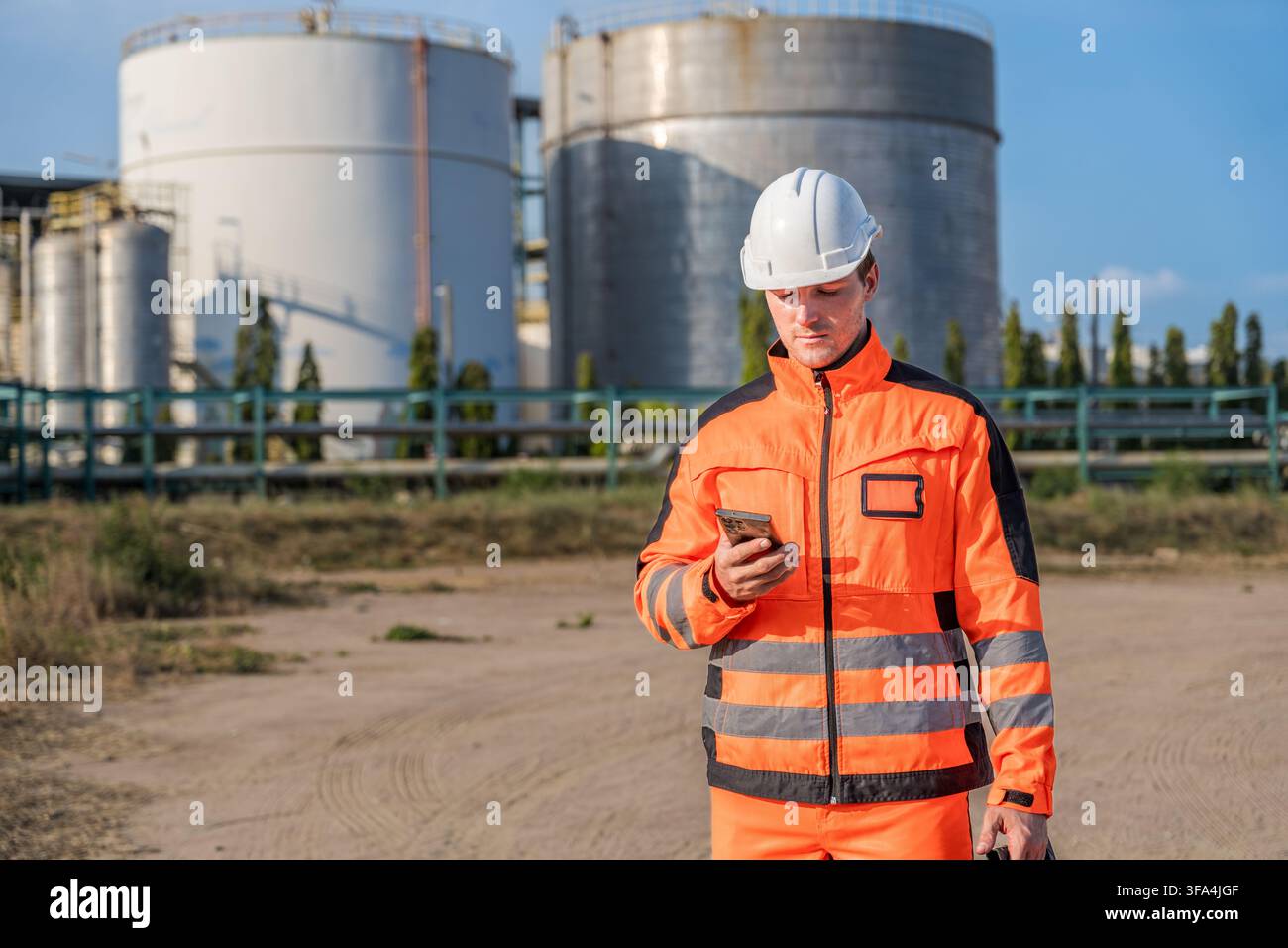 Bauarbeiter in Sicherheitsausrüstung, der auf einer Baustelle ein Smartphone zur Kommunikation verwendet. Ideal für Themen rund um Industrie, Technologie, Sicherheit und Arbeit Stockfoto