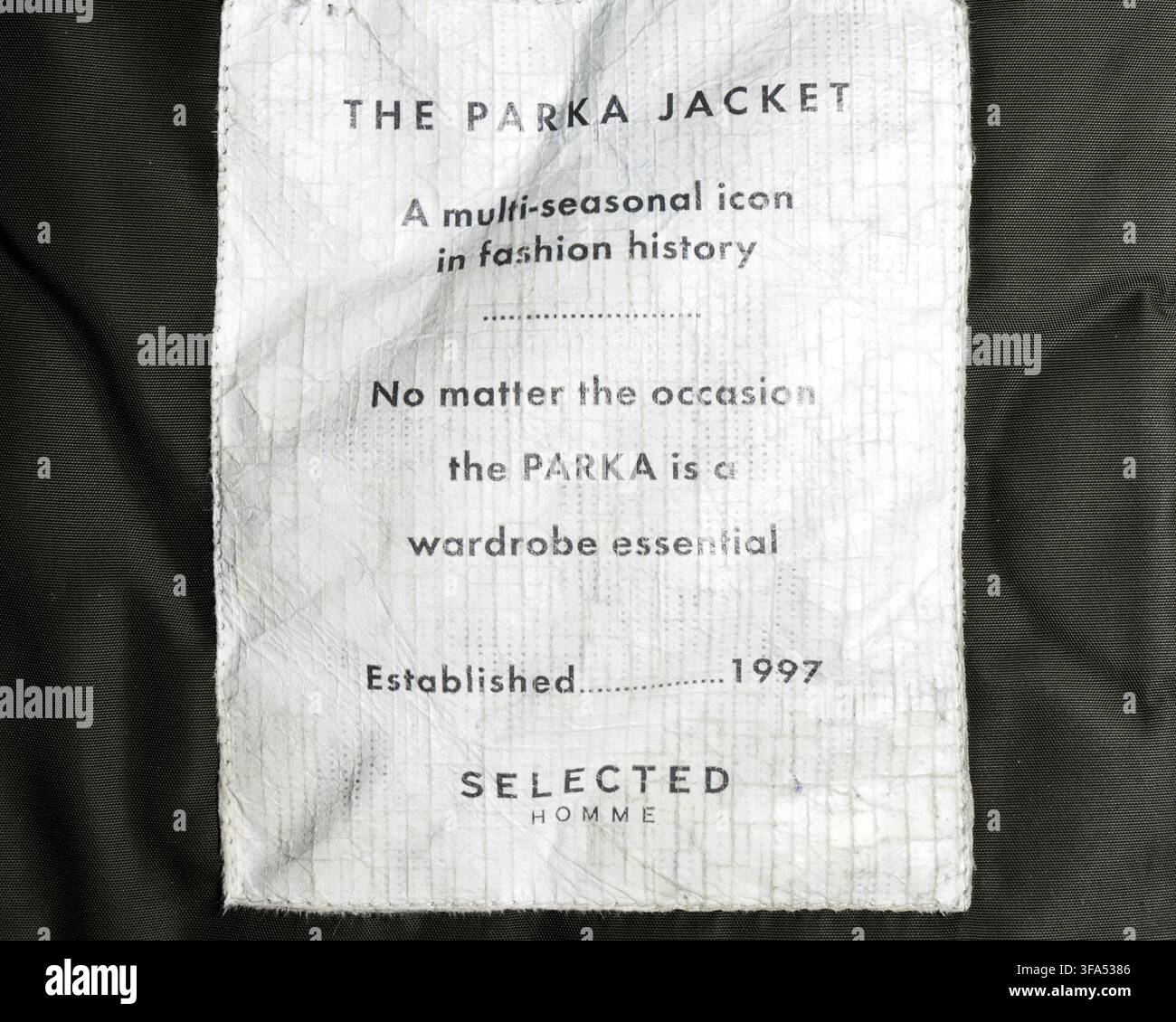 Ausgewähltes Homme Parkajacke-Label mit Werbetext, der das Kleidungsstück als unverzichtbares Kleidungsstück und vielseitiges Kleidungsstück für mehrere Jahreszeiten unterstreicht Stockfoto