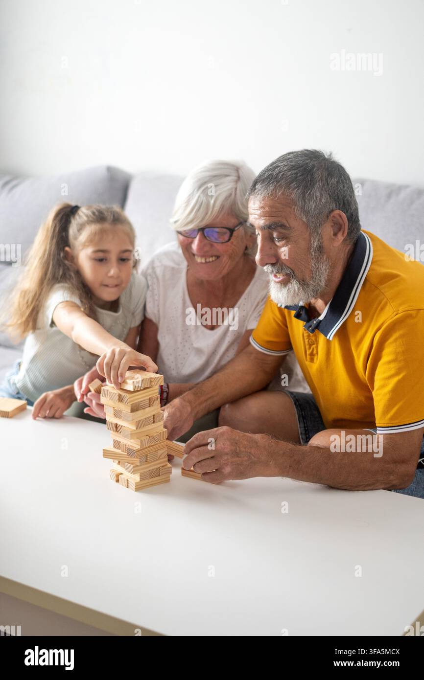 Zufriedene Großeltern spielen Holzklotzturm-Spiel mit ihren Enkelinnen zu Hause Stockfoto