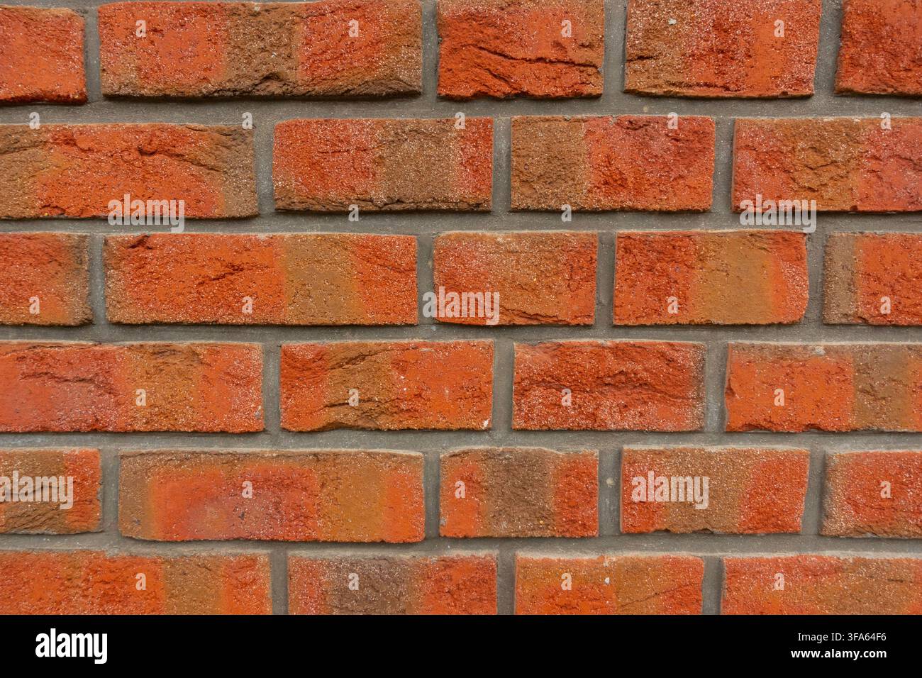 Nahaufnahme einer verwitterten roten Ziegelwand mit verschiedenen orange-roten Tönen, rauer Mauertextur und grauen Mörtelnahtstellen Stockfoto