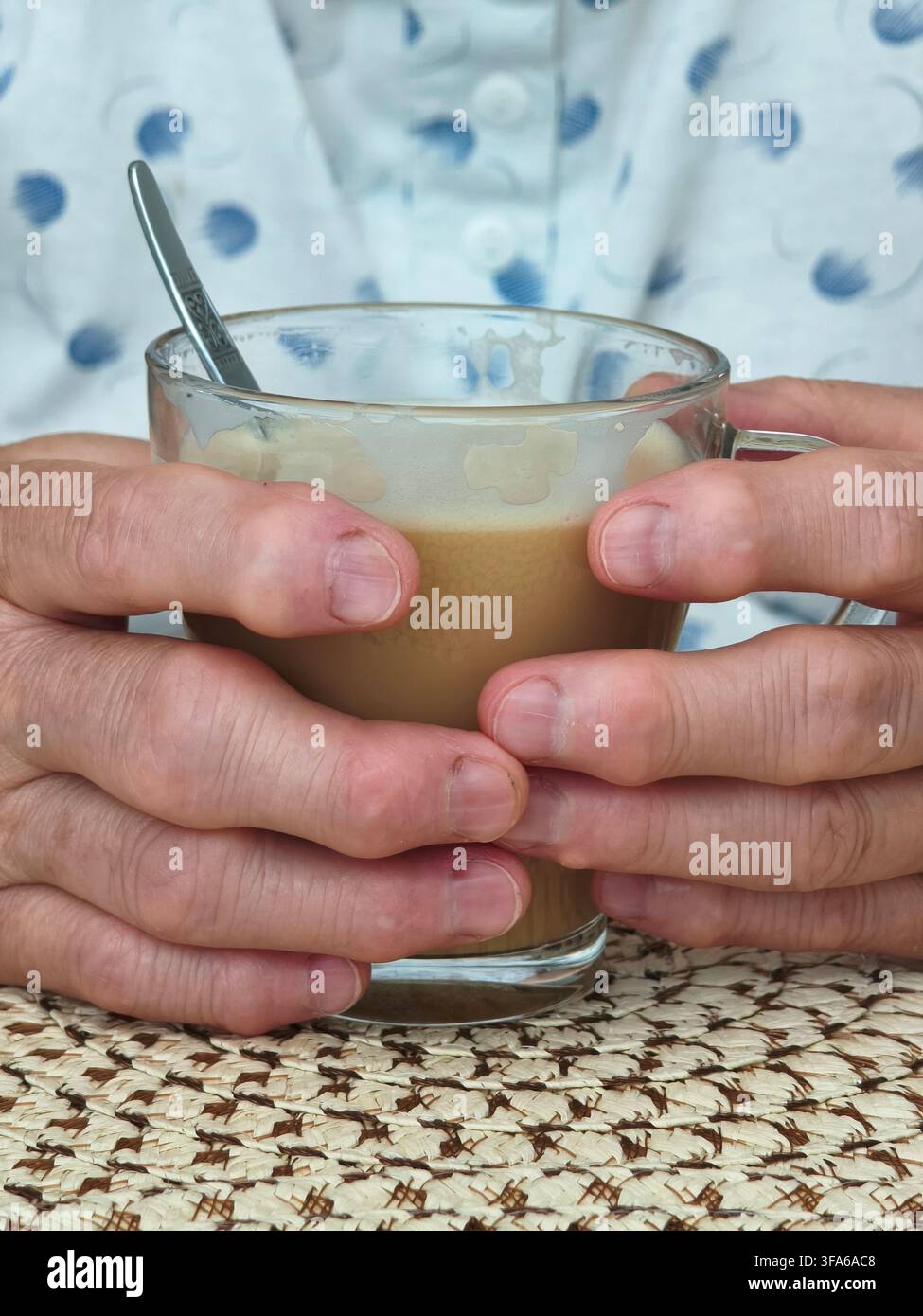 Nahaufnahme einer Person, die einen Glasbecher mit Kaffee und Milch in beiden Händen hält. - Smartphone-aufgenommenes Stockfoto