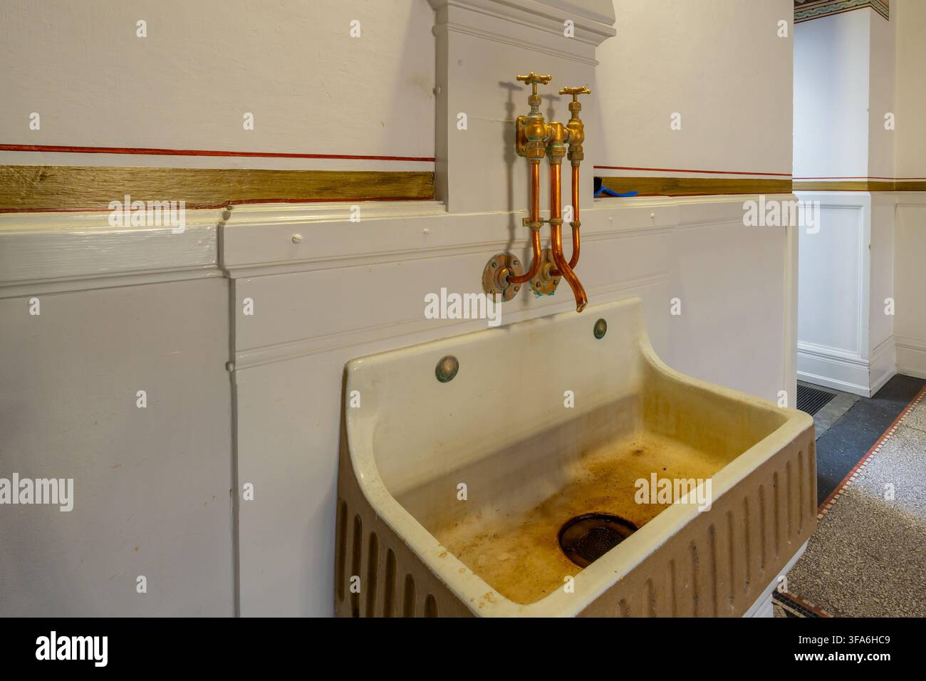 Ein antikes Waschbecken mit sichtbaren Abnutzungsspuren, das freiliegende Kupferrohre und ein klassisches Wasserhahndesign aufweist Stockfoto