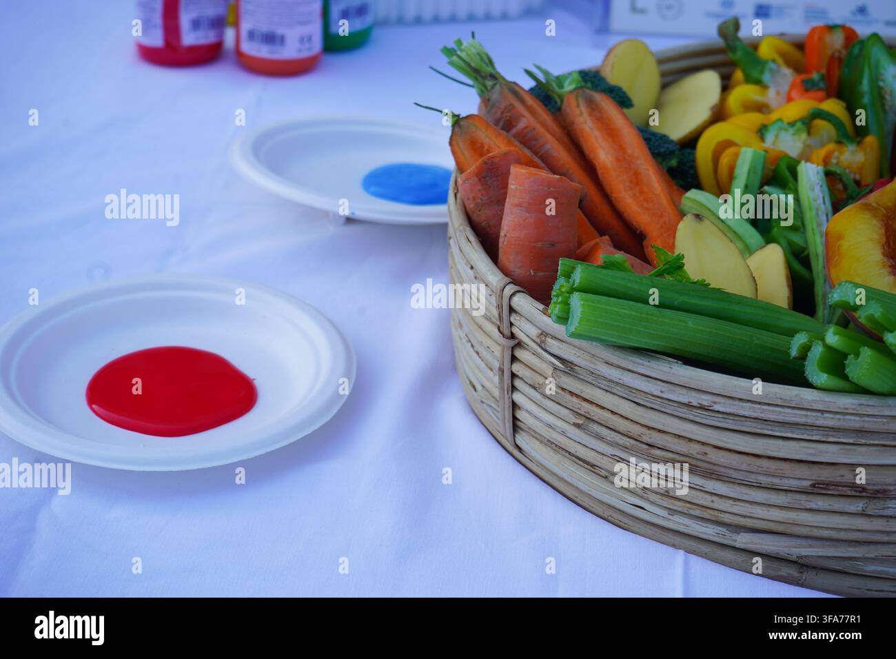Korb mit geschnittenem Obst und Gemüse neben bunten Farben auf Tellern, vorbereitet für eine Stempel-Kunstaktivität für Kinder. Stockfoto