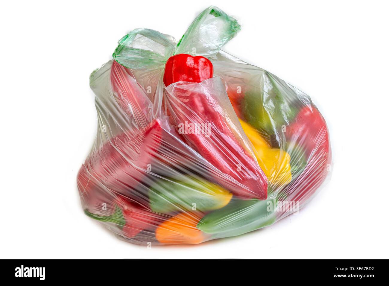 Eine durchsichtige Plastiktüte enthält rote, gelbe und grüne Paprika. Die Tüte ist oben zubunden. Stockfoto