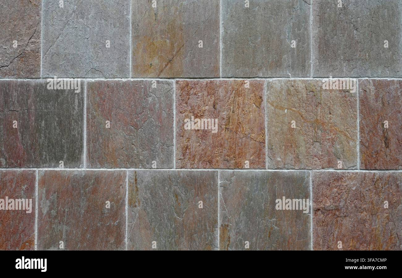 Horizontale Nahaufnahme einer mehrfarbigen quadratischen Ziegelwand mit gesprenkelten Ziegeln und glatten, gleichmäßigen Mörtel joints, die sichtbare Oberflächendetails zeigen Stockfoto