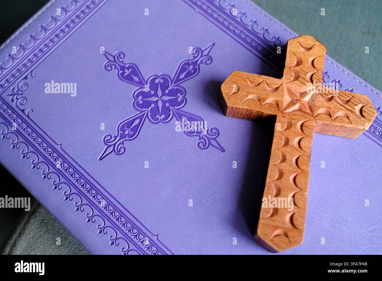Handgeschnitztes Holzkreuz auf einem violetten dekorativen religiösen Gebetsbuch. Stockfoto